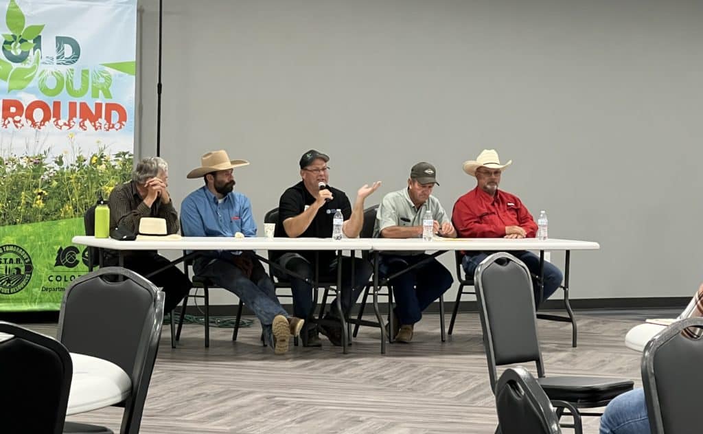 Five farmers sit at a table facing the crowd as part of a panel discussion on soil health.