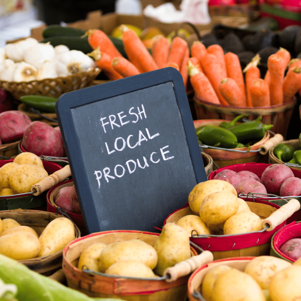 Chalkboard sign saying "Fresh Local Produce" surrounded by baskets of colorful vegetables