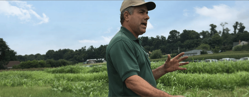 Steve Groff stands in a green field, mouth open as though speaking, hands gesturing